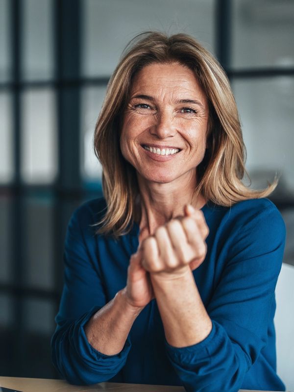 Smiling woman in a blue top showing her hand and looking at the camera.
