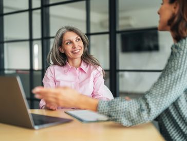 Two women engaged in a friendly office conversation.