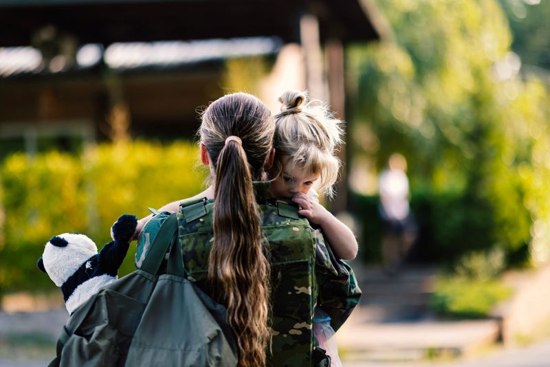 A woman, a mother, saying goodbye to her young daughter as she leaves for military service