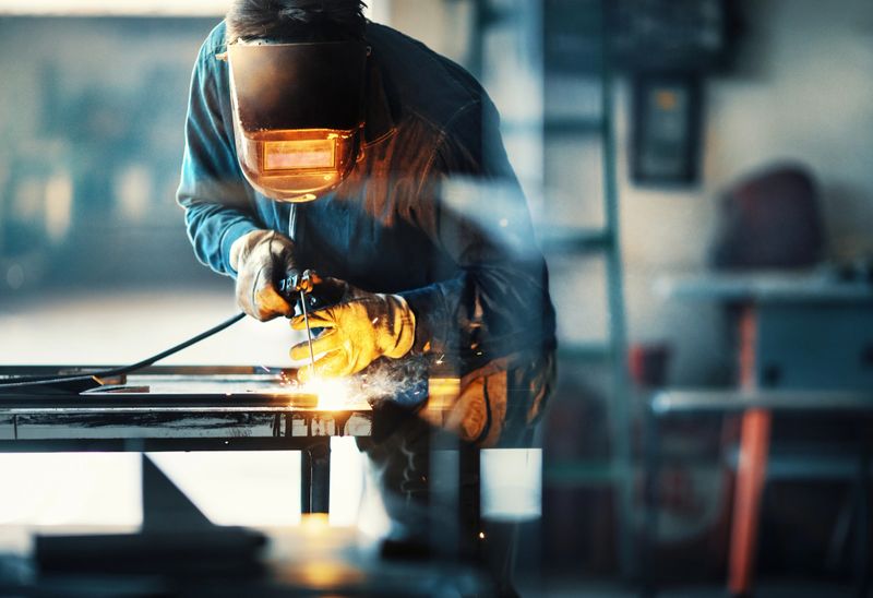 Closeup side view of unrecognizable worker welding two metal plates with gas welding machine.