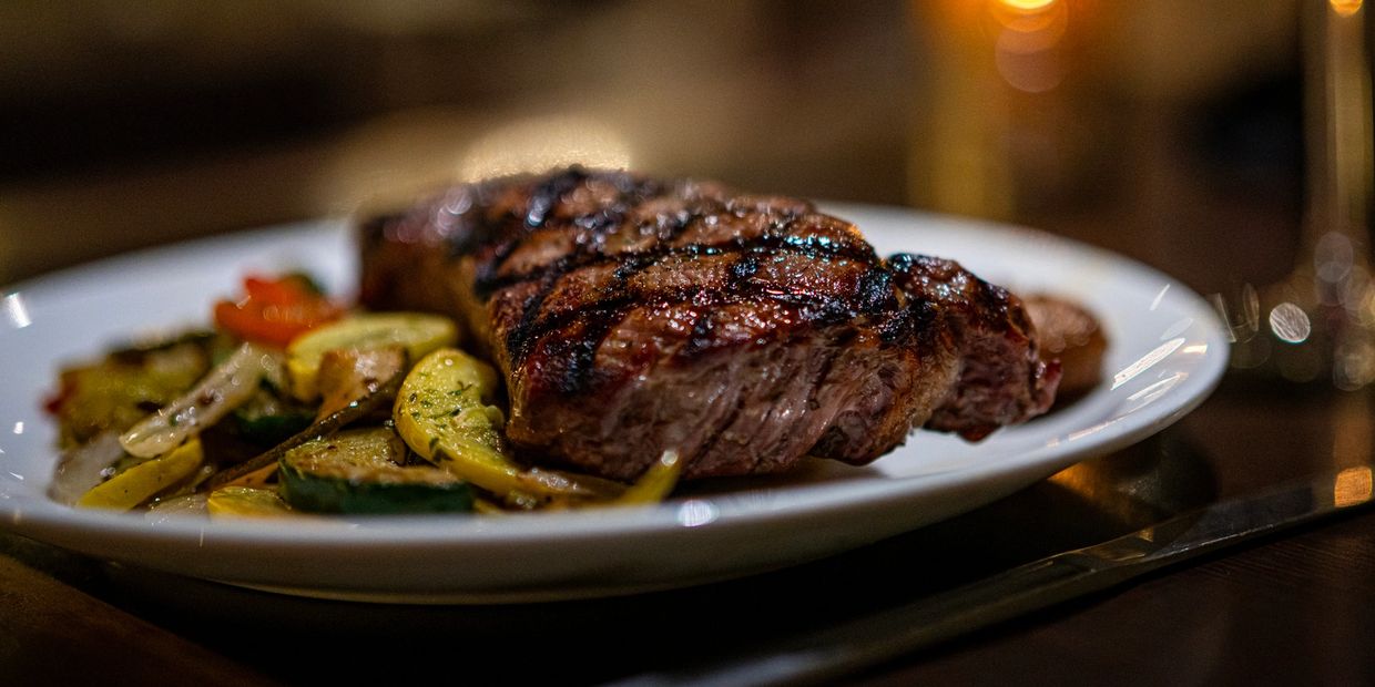 Grilled steak with vegetables on a white plate.