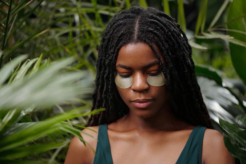 Portrait of woman with detox patches under eyes, surrounded by lush foliage, showcasing a moment of self-care and relaxation