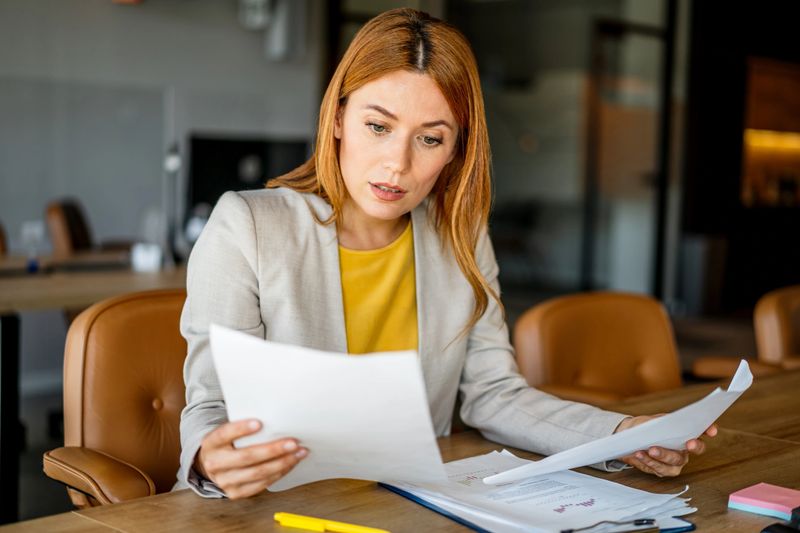 Focused businesswoman reviewing paperwork, analyzing financial reports and working with documents at her desk in a modern office