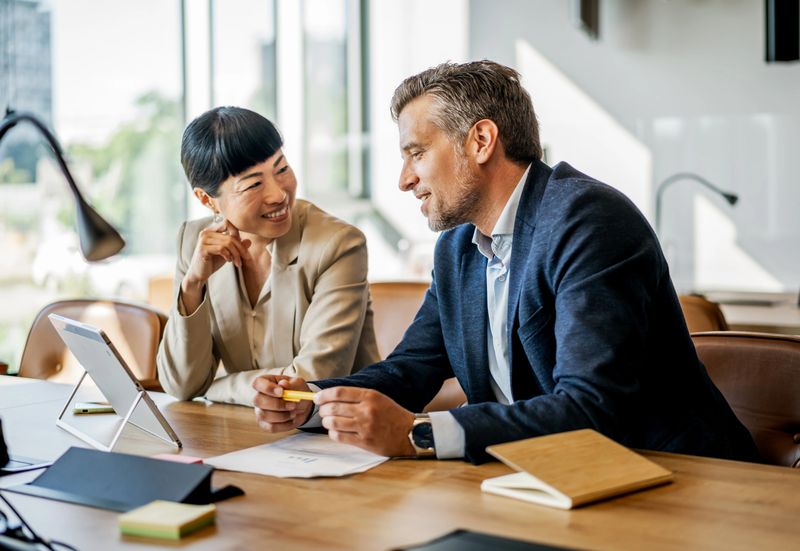 Two business people are discussing a project in a modern office, using a digital tablet and paperwork