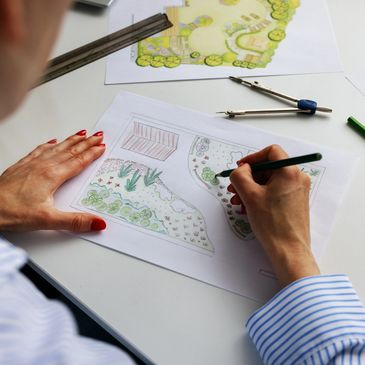Person sketching a garden landscape design with colored pencils and tools.