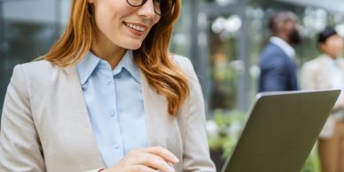 Smiling businesswoman using a laptop outdoors.