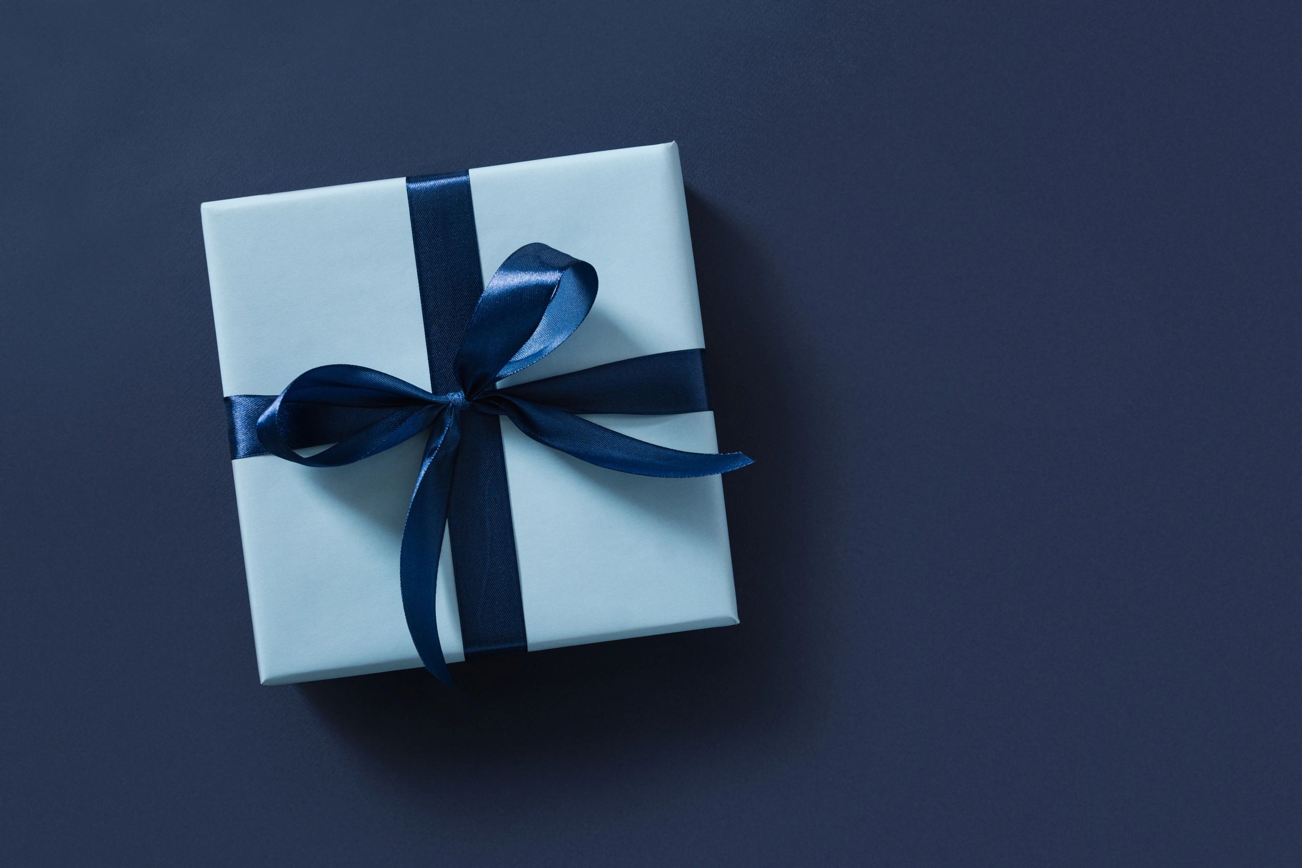 Blue gift box with dark blue ribbon on dark blue surface.