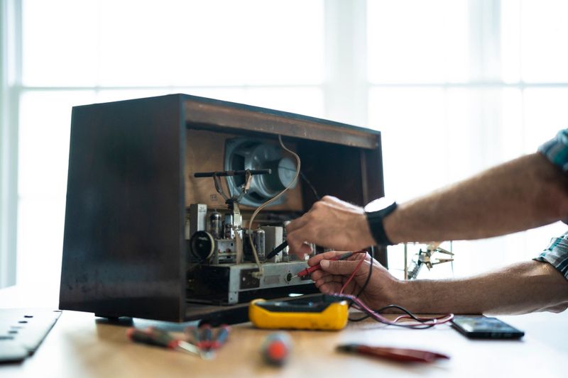 POV of electronics repairman is restoring vintage radio receiver using multimeter and smartphone. Upcycling, music love & retro tech fashion.