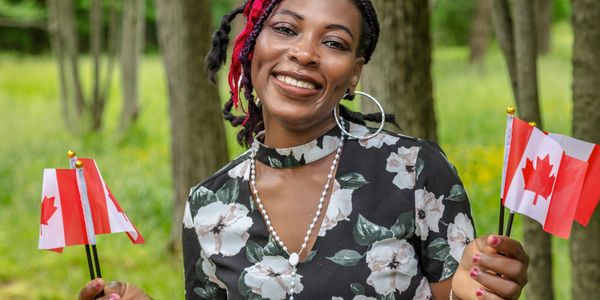 Femme noire tenant des drapeaux canadiens lors d’un rassemblement communautaire à Ottawa–Gatineau.