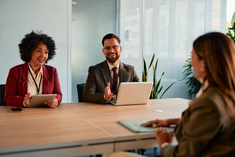 Human resources team conducting an interview with a young female candidate in a bright, modern office, sitting at a desk and sharing smiles while engaging in conversation
