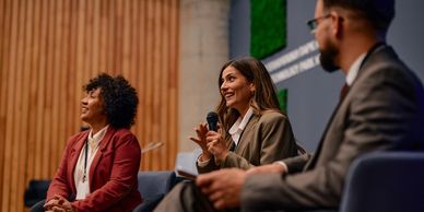Three professionals engaged in a panel discussion with a microphone and smiles.