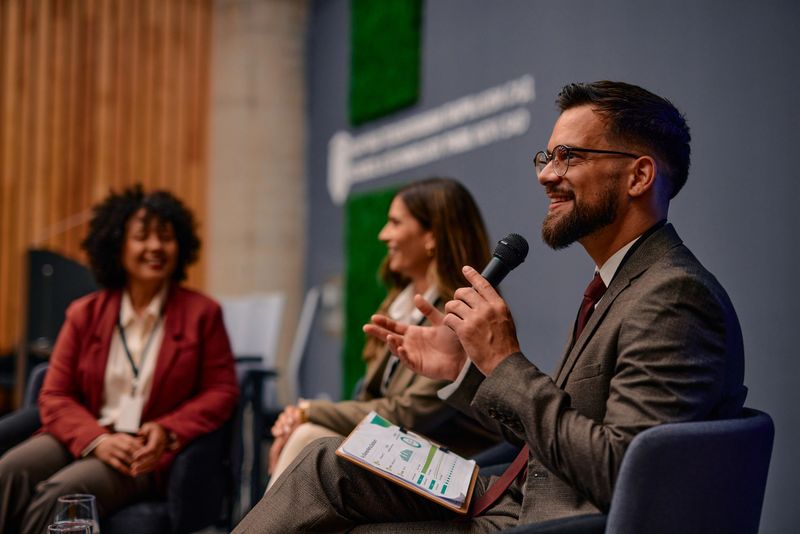 Businessman holding a microphone and gesturing while engaging with the audience during a panel discussion at a corporate conference, sharing insights on strategy and innovation