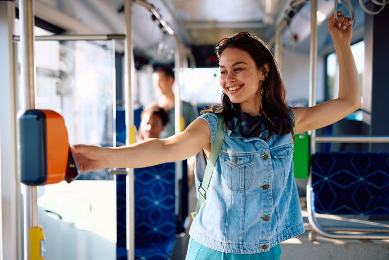 Young woman validating her bus ticket while holding onto a handrail, smiling brightly as she prepares for her journey on public transportation, embodying the spirit of urban life
