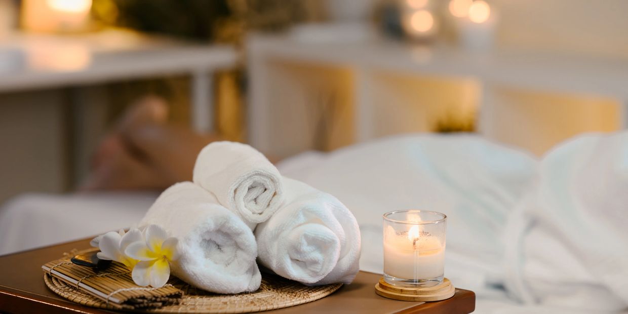 Rolled white towels and a lit candle on a spa table with relaxing ambiance.