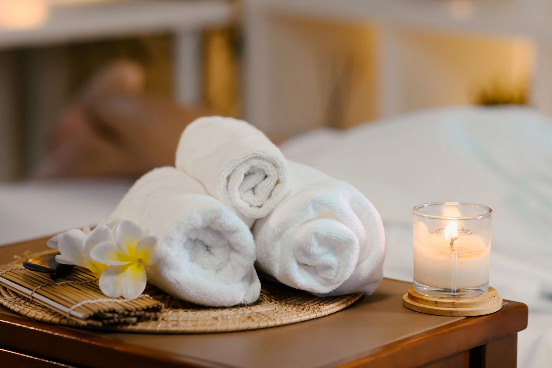 Rolled white towels with a lit candle and flowers in a spa setting.