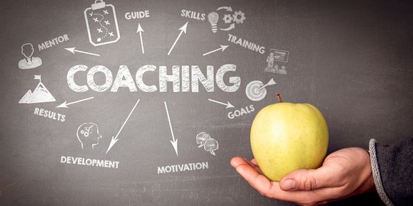 Hand holding an apple with coaching concepts on a chalkboard.