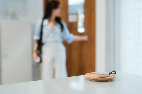 A woman opening a door with a key fob on a tray in the foreground.