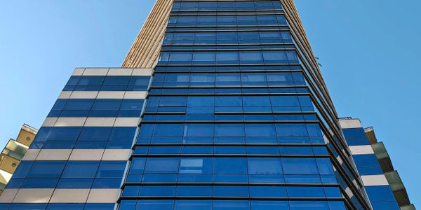 Upward view of a modern glass skyscraper against a clear blue sky.