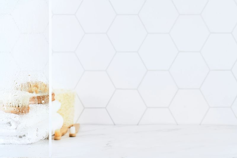 Marble table in bathroom with glass shower door with water droplets, towels, toothbrushes, sponges and body care comb in white. Minimal abstract background for product presentation. Design element.