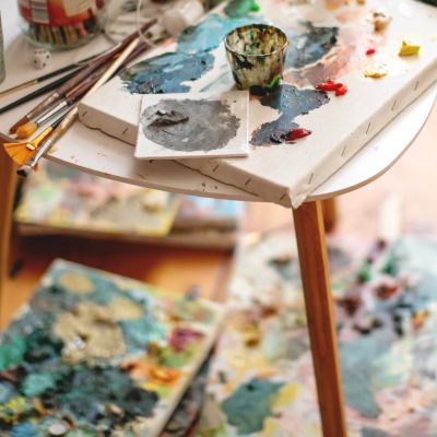 Artist's workspace with paintbrushes, palettes, and mixed colors on a table.