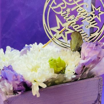 A floral birthday arrangement in a lavender box with a decorative sign.