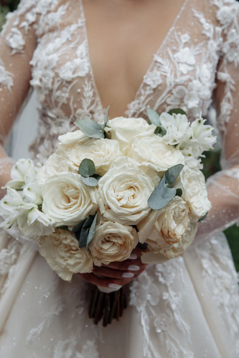 Close-up of bride in elegant wedding dress holding a delicate bouquet of white roses, pines and other beautiful flowers, romantic wedding atmosphere.