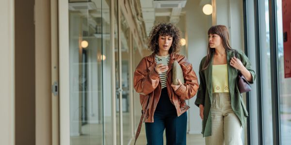 Two women walking and talking in a modern hallway.