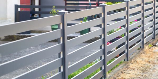 Modern gray metal fence with horizontal slats along a garden pathway.