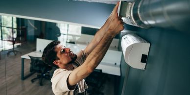 Man fixing ductwork on a wall.