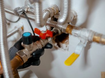 Close-up of gloved hand adjusting a valve in plumbing system.