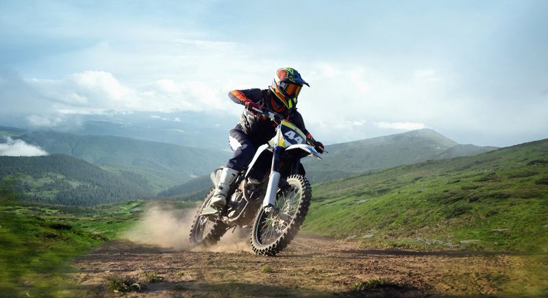 Professional biker in helmet speeds on mountain trail with dust and panoramic background of green hills. Concept of motorsport, speed, travel, adventure. 3D render of background. Composite image