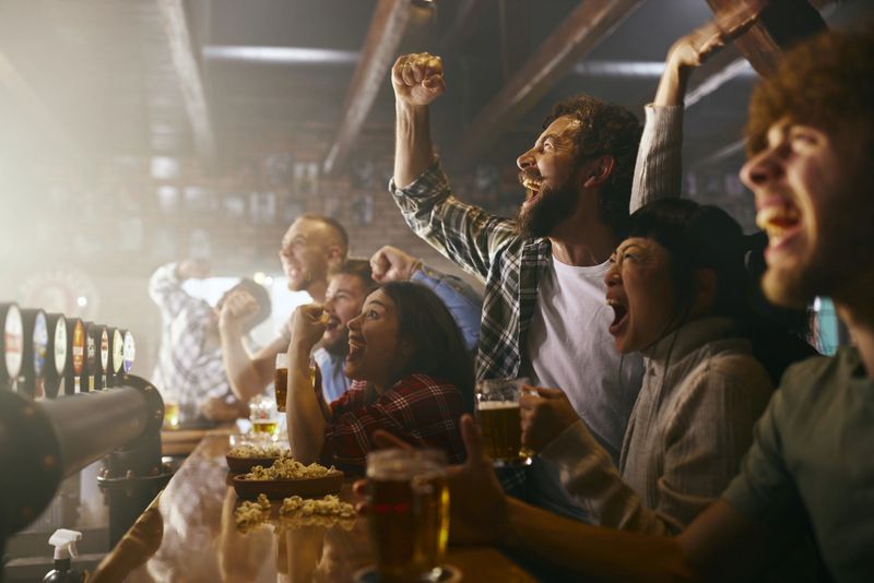 Cheerful sports fans having fun while celebrating victory of their team during a match on TV in a bar. Focus is on man with beard.