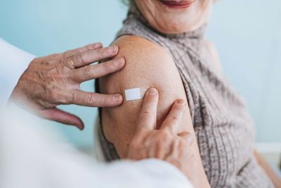 A doctor applies a small adhesive bandage to an elderly woman's upper arm after vaccination.
