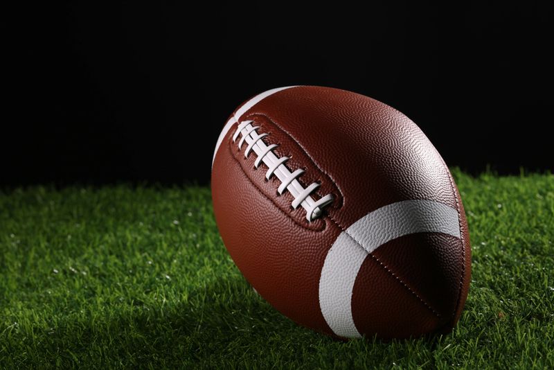 A textured American football resting on the green artificial turf with white line. College Football.