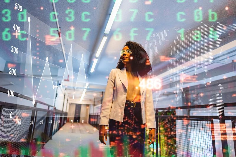 Stylish young woman wearing augmented reality glasses while walking through a high-tech office. Virtual charts, graphs, and digital data overlays create a dynamic atmosphere of innovation, finance, and modern technology.