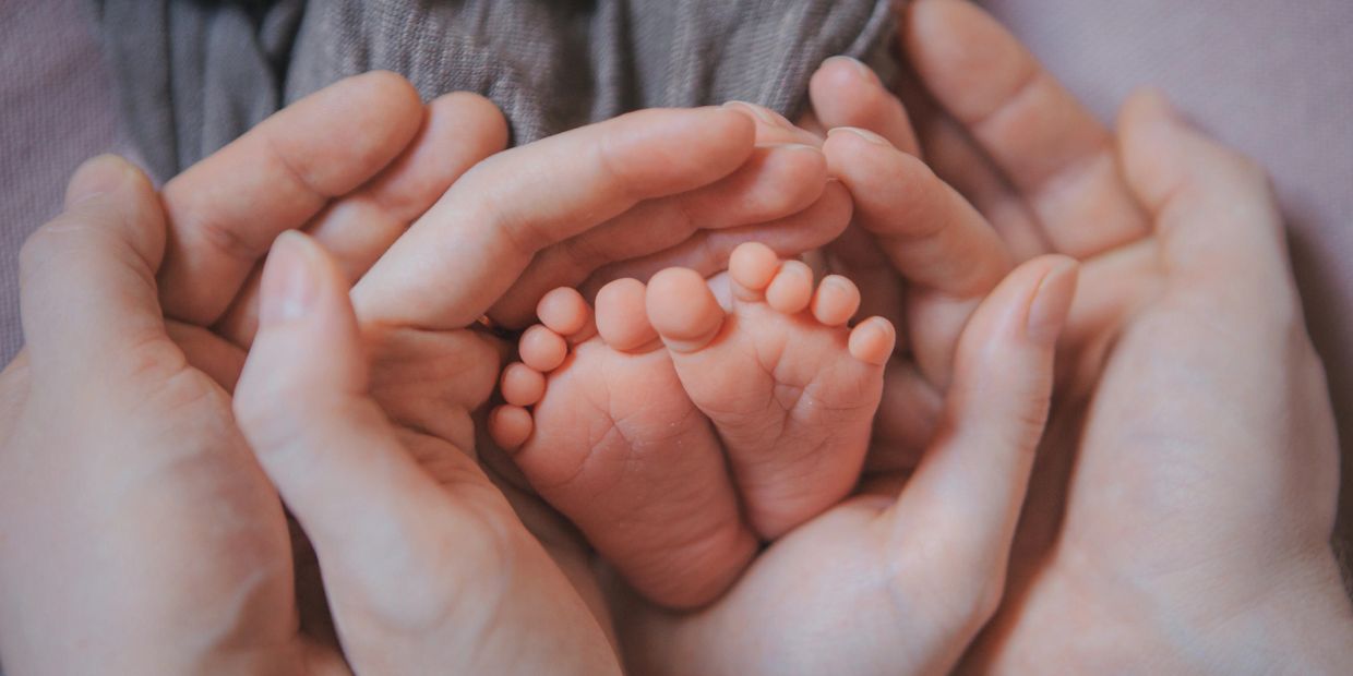 Adult hands gently cradling tiny baby feet in a heart shape.