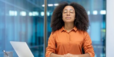 Woman meditating with eyes closed at a desk.