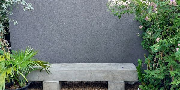 Minimalist concrete bench between potted plants on gravel.