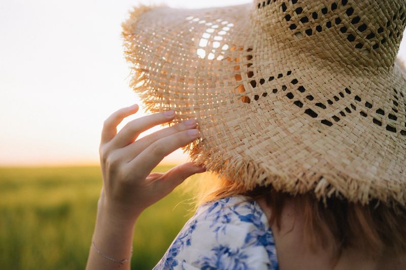 The close-up view of an unrecognisable woman’s hand wearing a straw hat at the nature in warm sunset setting