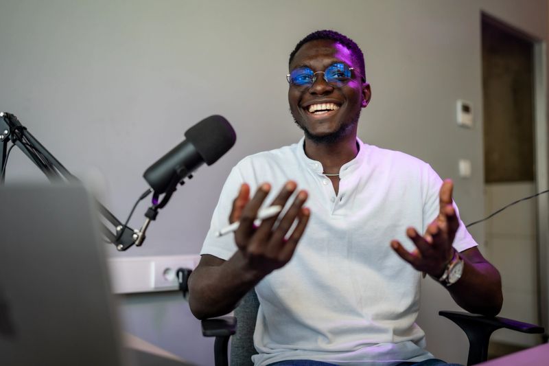 A smiling man enthusiastically records a podcast in a professional studio with a microphone setup.