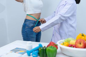 Doctor measures a woman's waist with a tape.