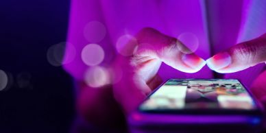 Person using smartphone in purple light.
