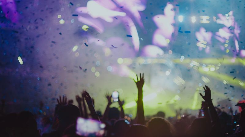 Crowd dancing and cheering at a festival concert while glitter is falling from above.