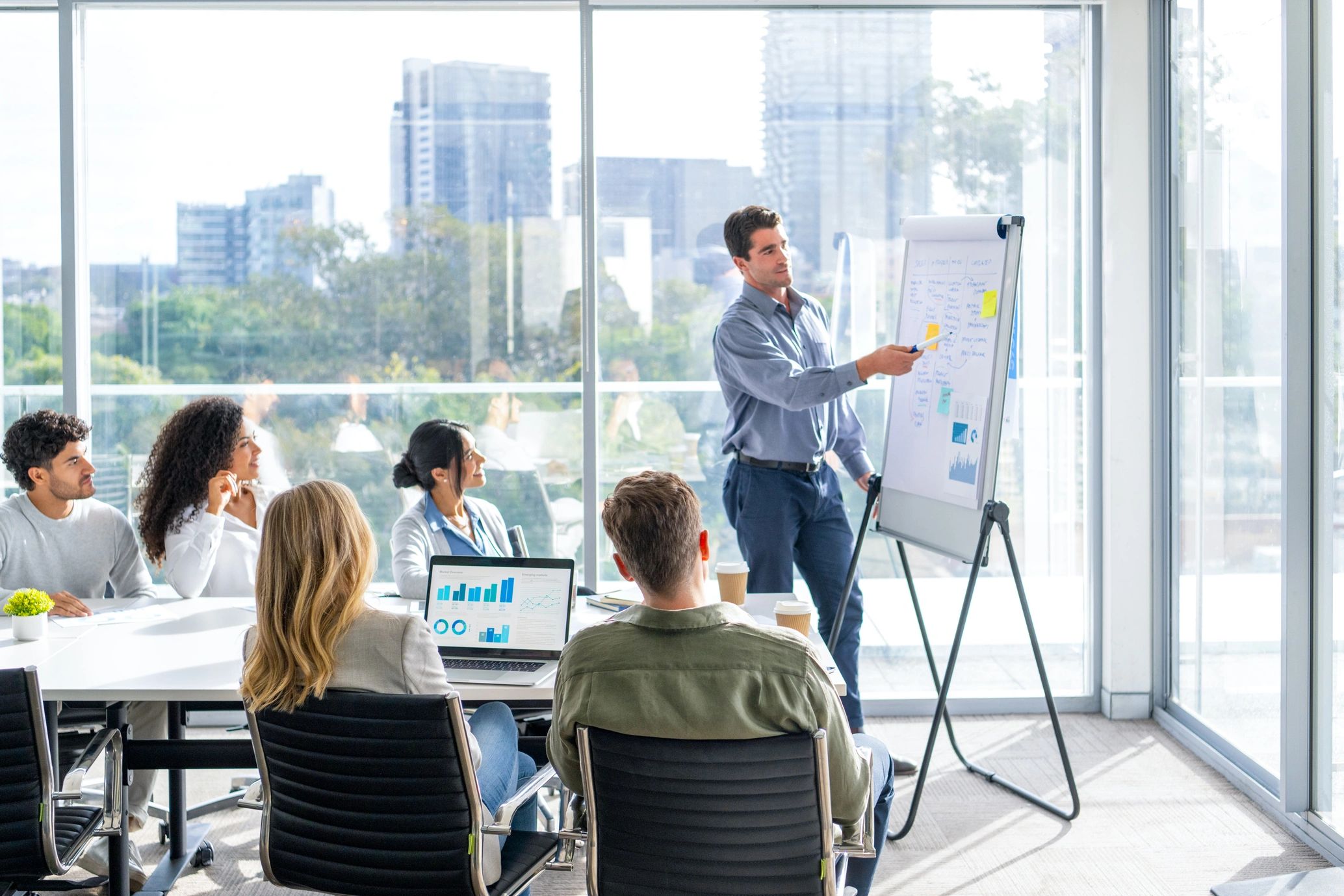 Man presenting data to colleagues in a modern office with city view.