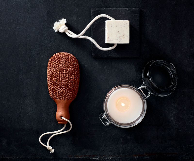Candle, foot brush, and soap arranged on a black background
