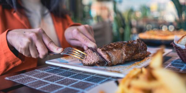 Person slicing a juicy steak at a restaurant.