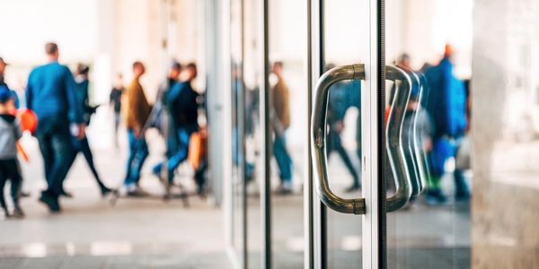 Close-up of glass door handles with blurred crowd walking in background.