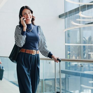 A stylish woman talking on phone while holding a suitcase in an airport.