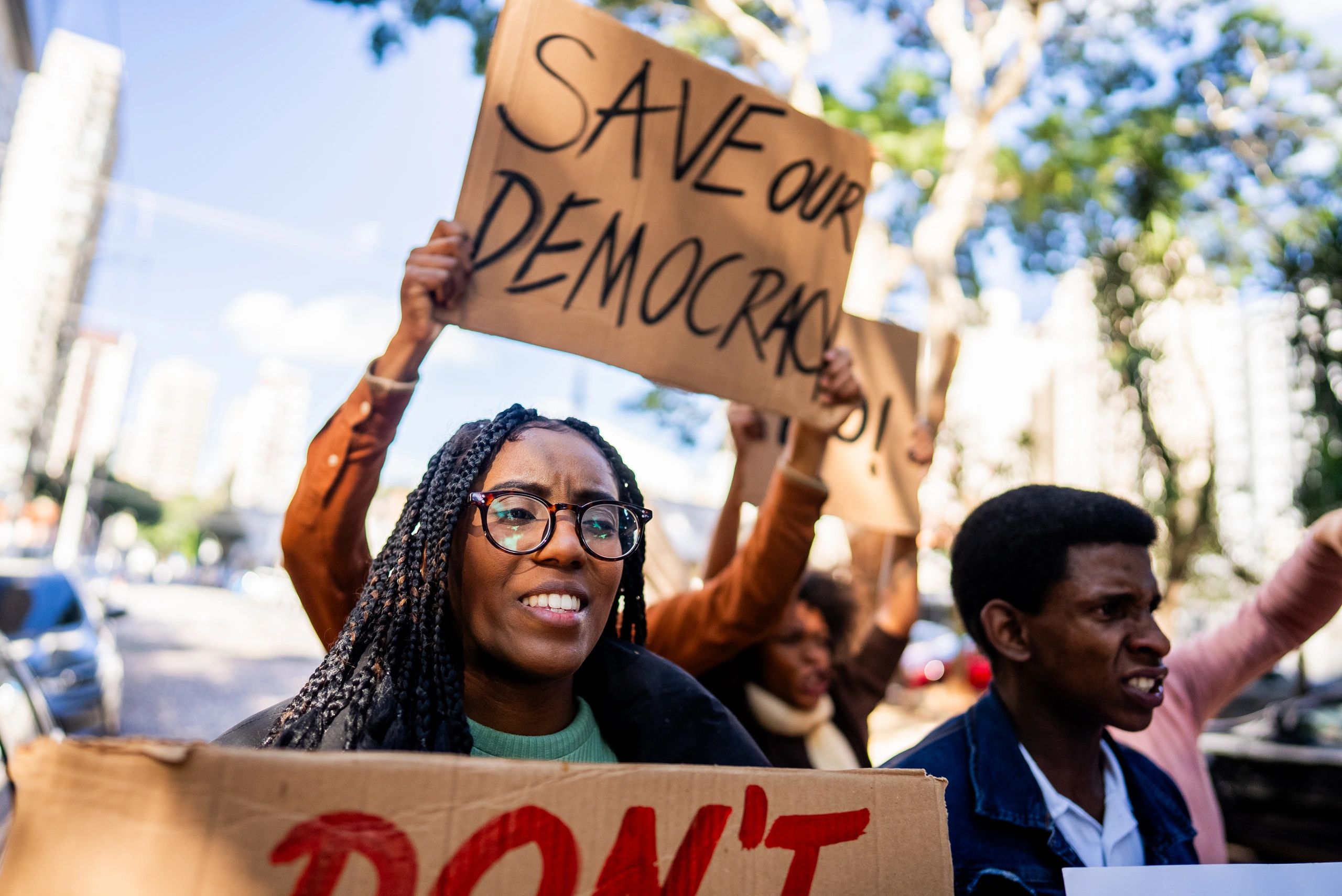 Protesters holding signs demanding to save democracy outdoors.