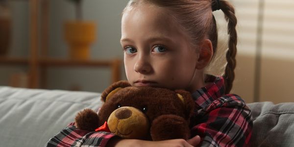 A young girl hugging a teddy bear with a thoughtful expression.